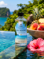 Bottle of Bali Reserve Island Collection oil with a tropical setting featuring a pool, pineapple, and flowers.