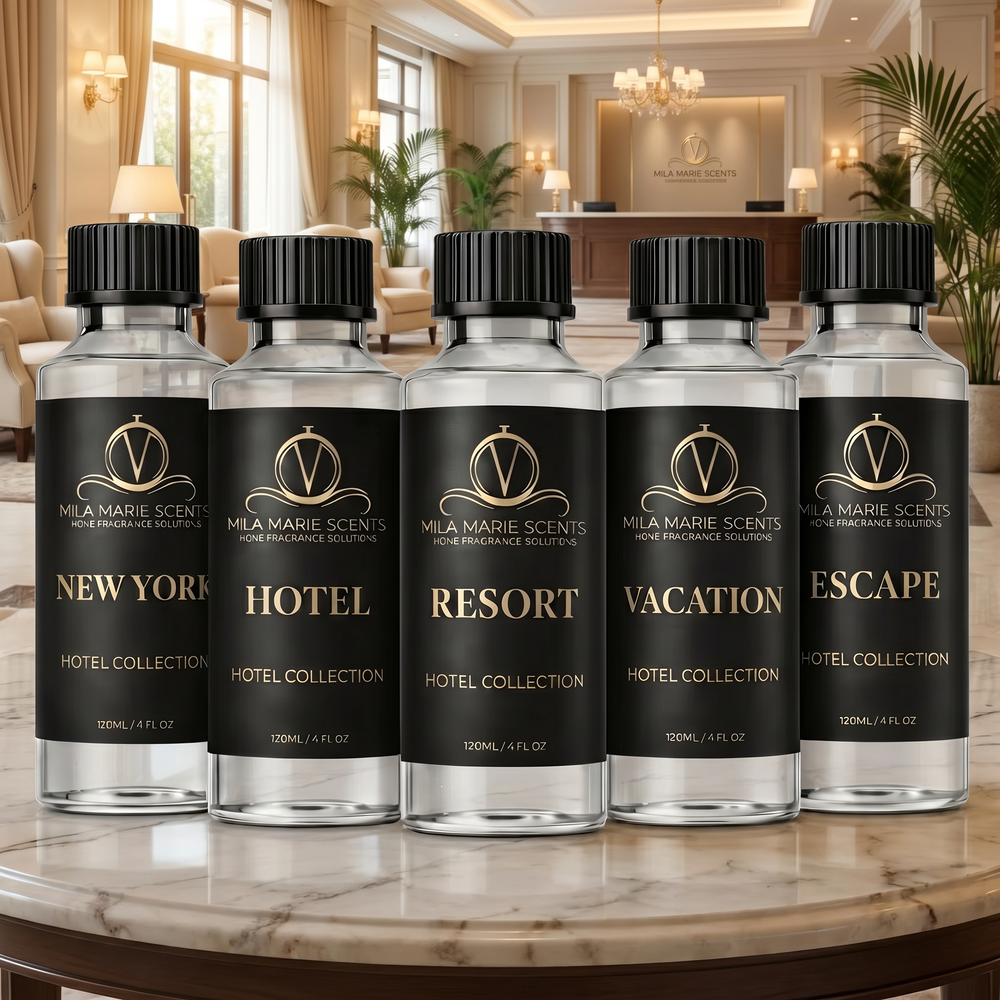 Five bottles of Mela Marie Scents home fragrance solution on a marble table with a luxurious hotel lobby in the background.